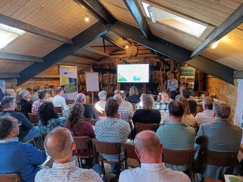 Deelnemers in een zaal, kijkend naar een presentatie